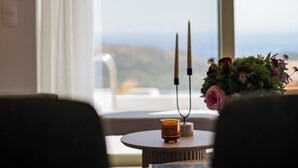 A room with a view through a large window, a table with a candle and a book, and a vase with flowers. - Hillside Villa with Private Pool & Panoramic Views | Plakias & Preveli (Asomatos)