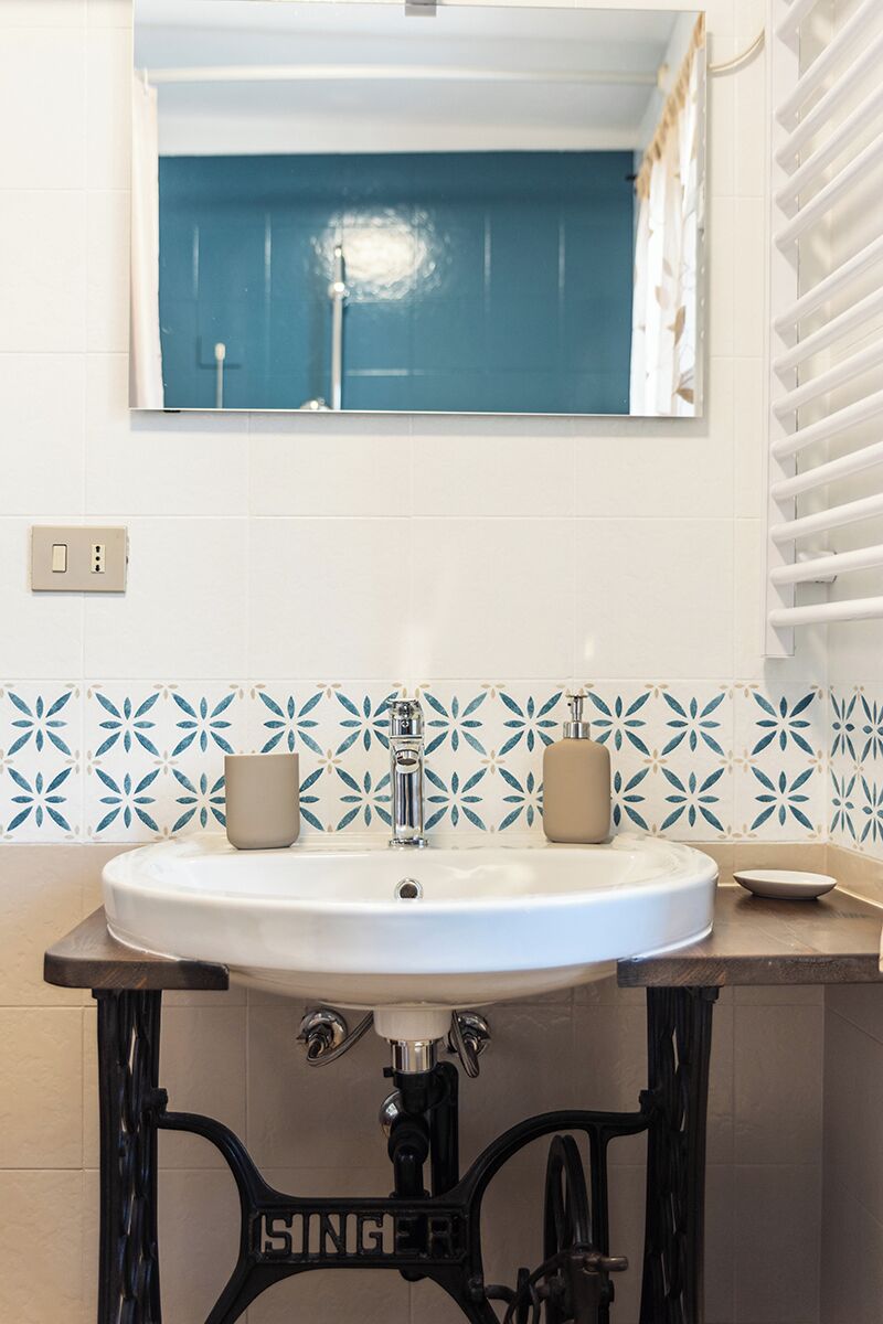 Un baño con un lavamanos blanco, un espejo encima y una pared con azulejos azules.