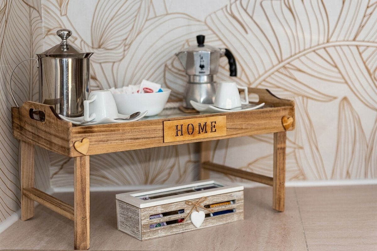 Une petite table en bois, sur laquelle on a posé un plateau décoratif avec le mot «MAISON», une cafetière, des tasses et une boîte de magazines.