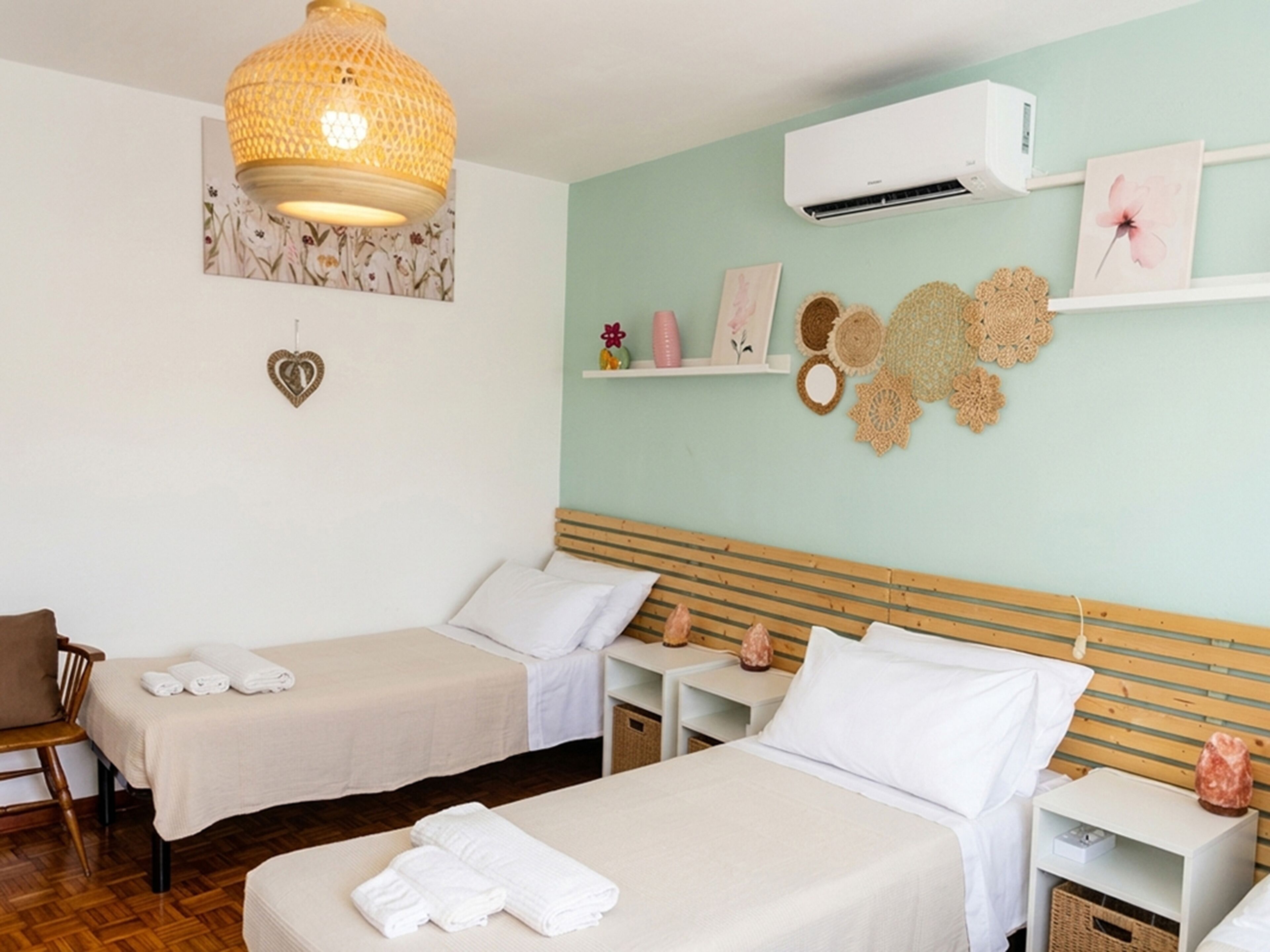 Habitación de hotel con dos camas, cabecera de madera, aire acondicionado instalado en la pared, lámpara colgante y decoración en la pared.