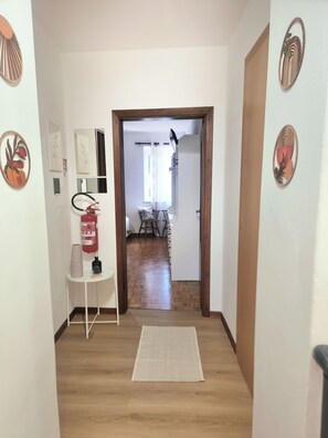 A hallway with a fire extinguisher, a small table with cups, and a mat on the floor.