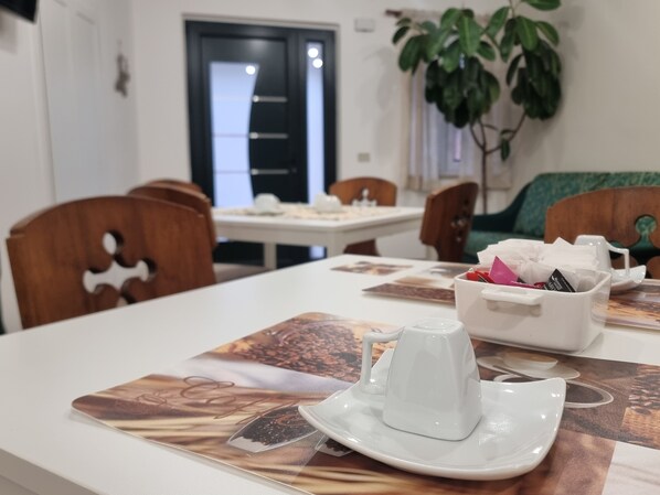 A dining area with a table set for two, a white coffee cup, and a plant in the background.