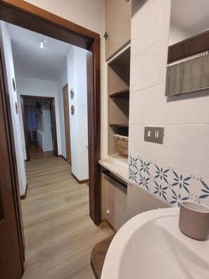 A bathroom with a sink, mirror, and shelves.