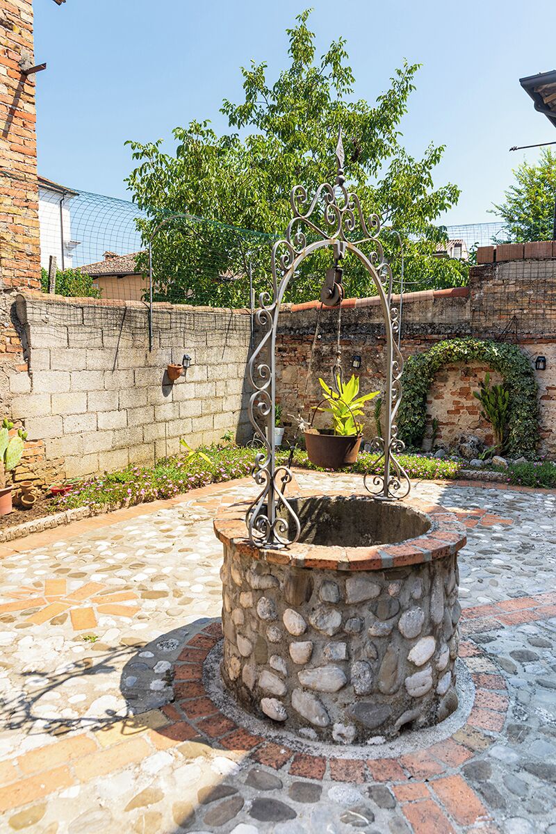 Una jardinera de piedra con una planta colgante, rodeada por un patio adoquinado.