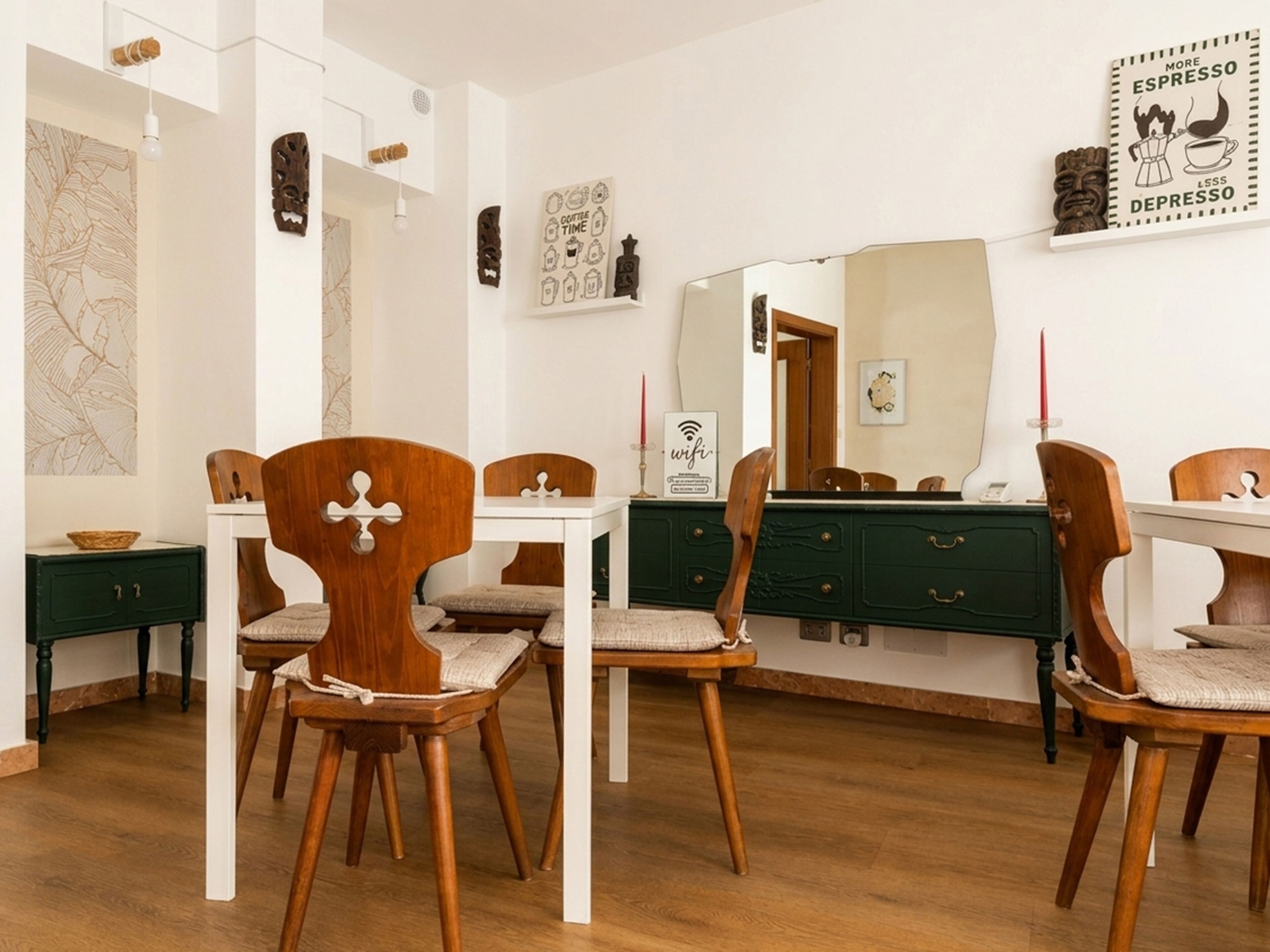 Un coin repas avec des chaises en bois et une table blanche, un meuble vert et un mur orné d’un miroir et d’œuvres d’art.