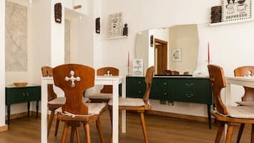 Un coin repas avec des chaises en bois et une table blanche, un meuble vert et un mur orné d’un miroir et d’œuvres d’art.