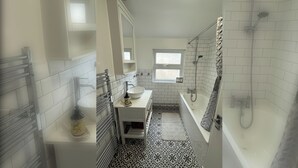 Un baño estrecho con un lavamanos blanco, un espejo, una ventana y una ducha.