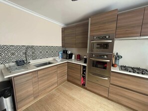 Eine moderne Küche mit Holzschränken, einer Edelstahlspüle, einem Einbauofen und einem Gasherd.