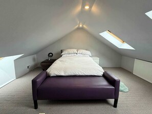 Ein Schlafzimmer mit Bett, Nachttisch, Lampe und Fenster.