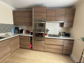 A compact kitchen with built-in appliances, wooden cabinets, and a tiled backsplash. - Chic Victorian Home in Forest Gate (Greater London)