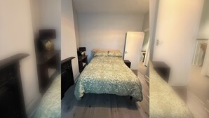 Un pasillo estrecho que da a un dormitorio con cama, mesitas de noche y un pequeño mueble auxiliar.