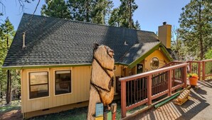 A cabin with a sloped roof, a deck, and a wooden sculpture.