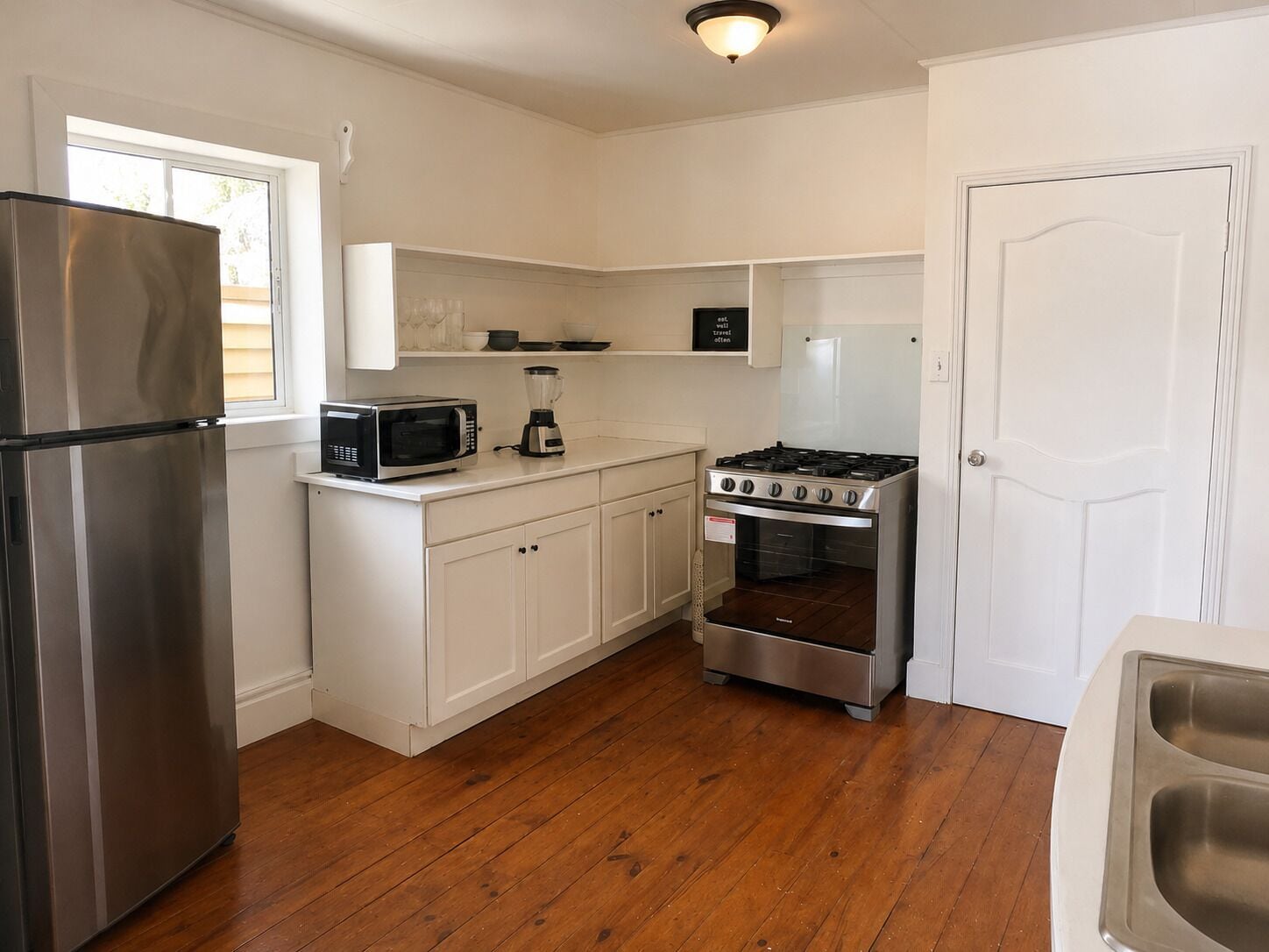 A kitchen with a stainless steel refrigerator, a microwave, a blender, a stove, and an oven.