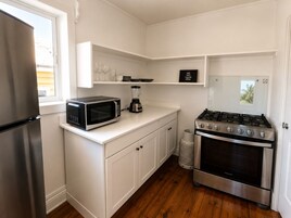 A compact kitchen with a stainless steel refrigerator, a microwave, a gas stove, and white cabinetry.