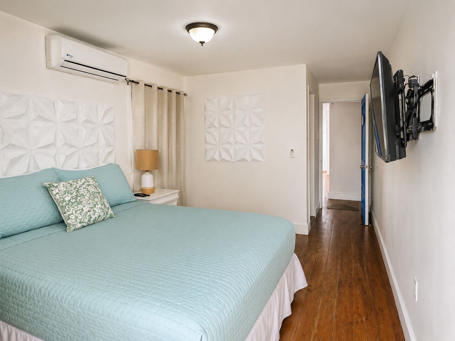 Un dormitorio con cama, mesita de noche, televisor montado en la pared y aire acondicionado.