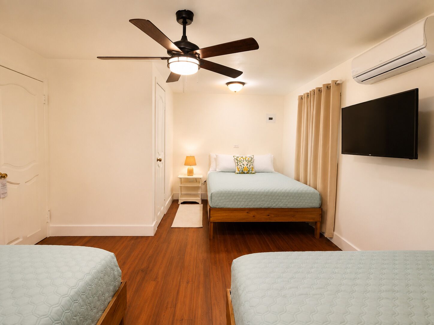 A hotel room with a bed, a nightstand, a lamp, a ceiling fan, an air conditioning unit, and a television.
