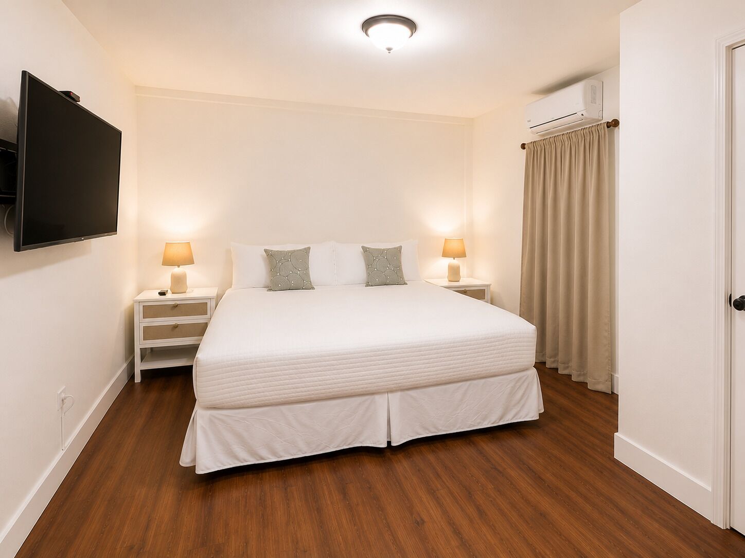 Ein Hotelzimmer mit einem großen Bett, zwei Nachttischen mit Lampen, einem wandmontierten Flachbildfernseher und einer Klimaanlage.