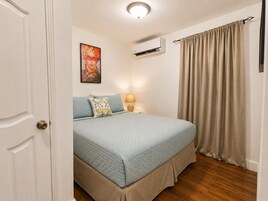 Un dormitorio con cama, un cuadro, un equipo de aire acondicionado y una ventana con cortinas.