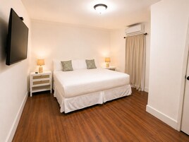 A hotel room with a bed, two bedside tables, a flat-screen TV, and an air conditioning unit.
