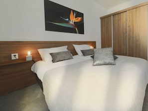 Een net opgemaakt bed met een houten hoofdbord, een aan de muur bevestigd lampje en een lijst met een afbeelding erboven.