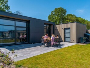 Een terras met een modern gebouw, een klein constructie en een gazon.