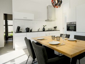 Een moderne keuken met witte kasten, een houten eettafel en een bijzondere geometrische hanglamp.