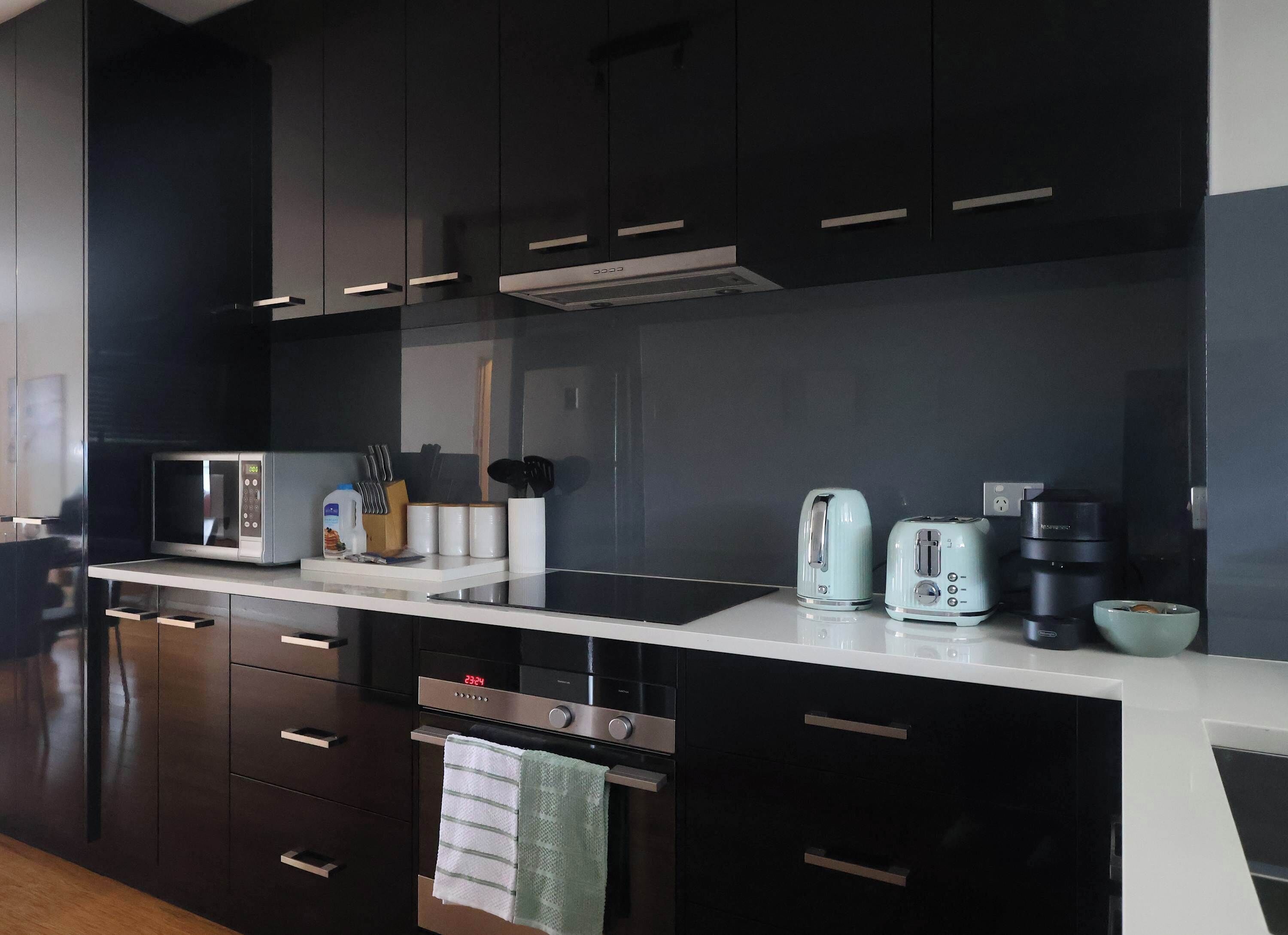 Una cocina moderna con armarios oscuros, encimera blanca, microondas, tostadora, cafetera y pileta.