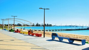 A beach promenade with benches, a pier, and boats in the background. - Rockingham Retreat | Right By The Beach (Rockingham)