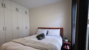 A bedroom with a bed, a wardrobe, a bedside table with a plant, and a curtain. - Rockingham Retreat | Right By The Beach (Rockingham)