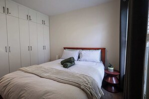 A bedroom with a bed, a wardrobe, a bedside table with a plant, and a curtain. - Rockingham Retreat | Right By The Beach (Rockingham)