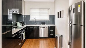 A modern kitchen with a dishwasher, stainless steel appliances, and a trash bin. - Rockingham Retreat | Right By The Beach (Rockingham)