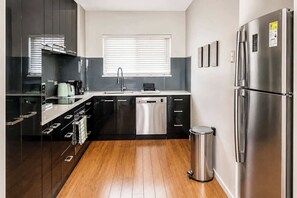 A modern kitchen with a dishwasher, stainless steel appliances, and a trash bin. - Rockingham Retreat | Right By The Beach (Rockingham)