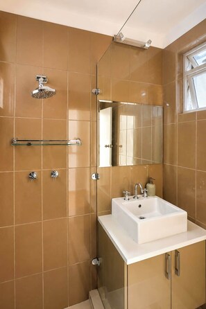 Een badkamer met een witte wastafel, een douchecabine van glas en een spiegel.