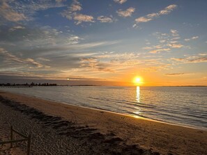 A beach with a sunset, calm water, and a pier in the distance. - Rockingham Retreat | Right By The Beach (Rockingham)