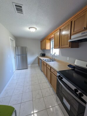 A kitchen with a stainless steel refrigerator, wooden cabinets, a black stove, and a window with a plant.