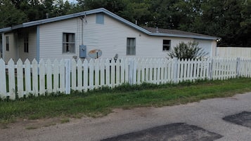 A single-story house with a white picket fence, a satellite dish, and a gravel driveway.