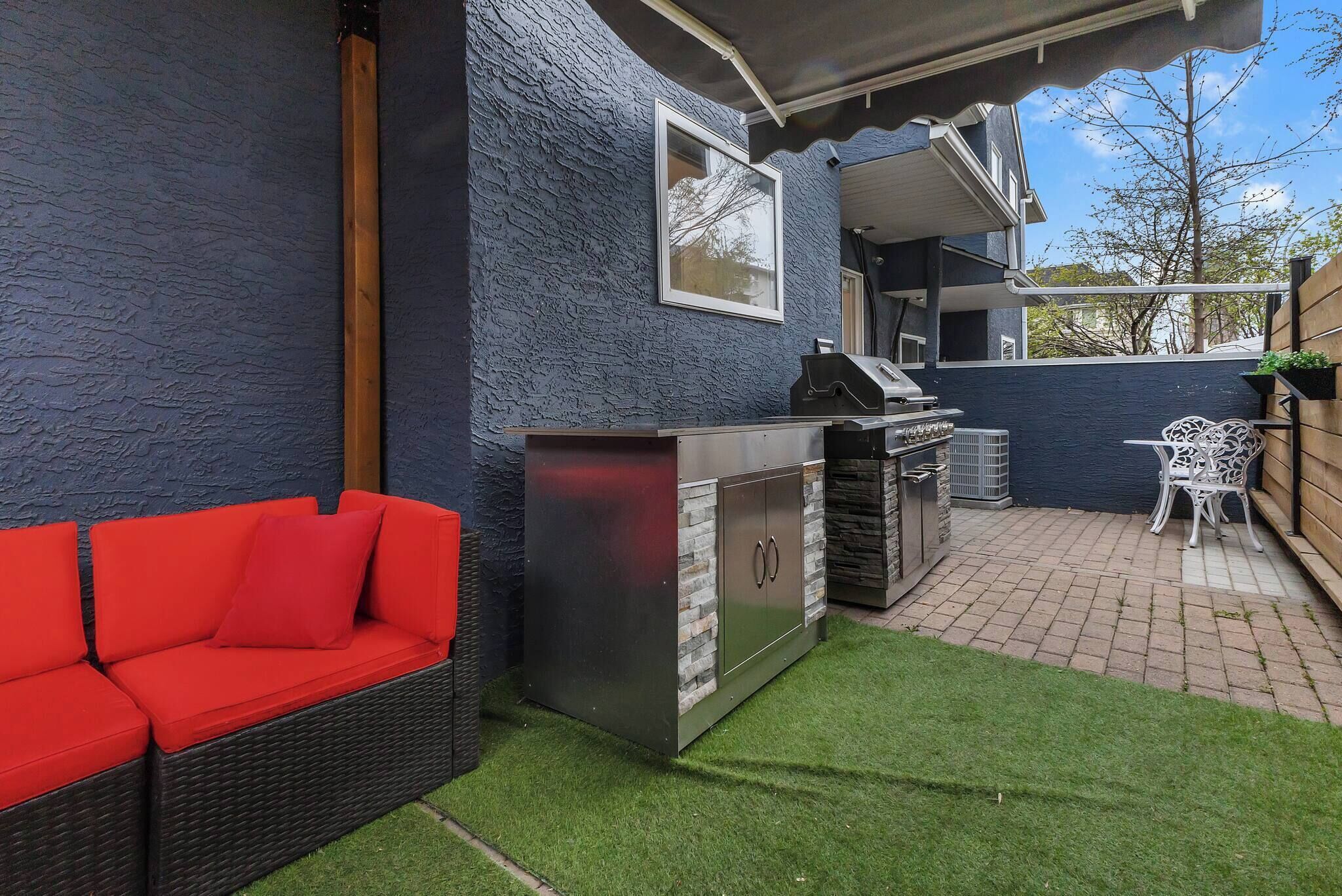 A patio with a grill, a red sofa, and a small table.