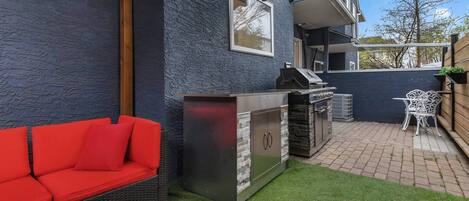 A patio with a grill, a red sofa, and a small table.