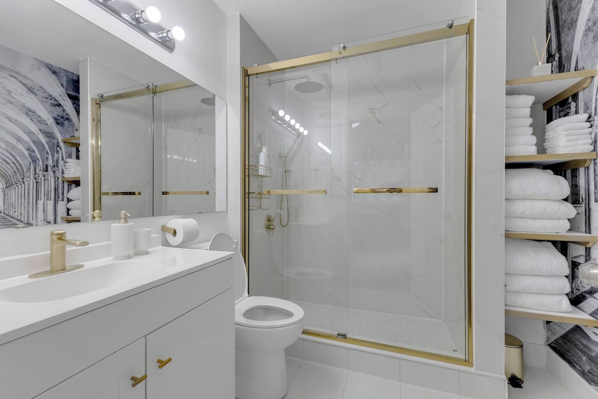 A modern bathroom with a glass-enclosed shower, a white sink with gold fixtures, and a marble-tiled wall.