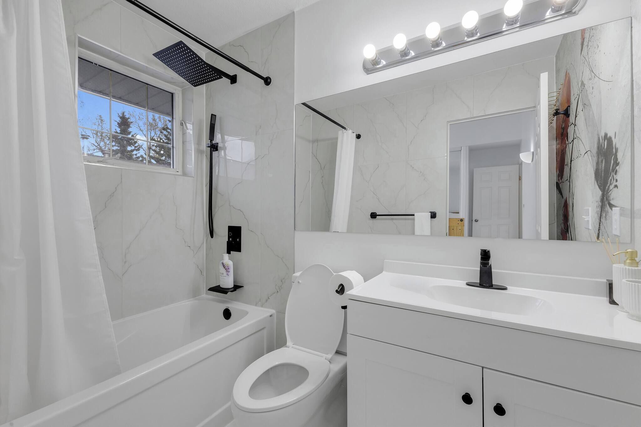 A modern bathroom with a bathtub, toilet, vanity, and a large mirror.