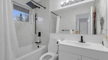A modern bathroom with a bathtub, toilet, vanity, and a large mirror.