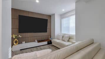 Una sala de estar moderna con un televisor de pantalla plana, un sofá, una consola blanca y una ventana con persianas.