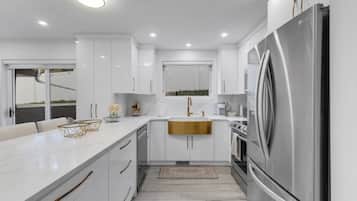 Una cocina moderna con muebles blancos, un refrigerador de acero inoxidable y una isla grande con encimera dorada.