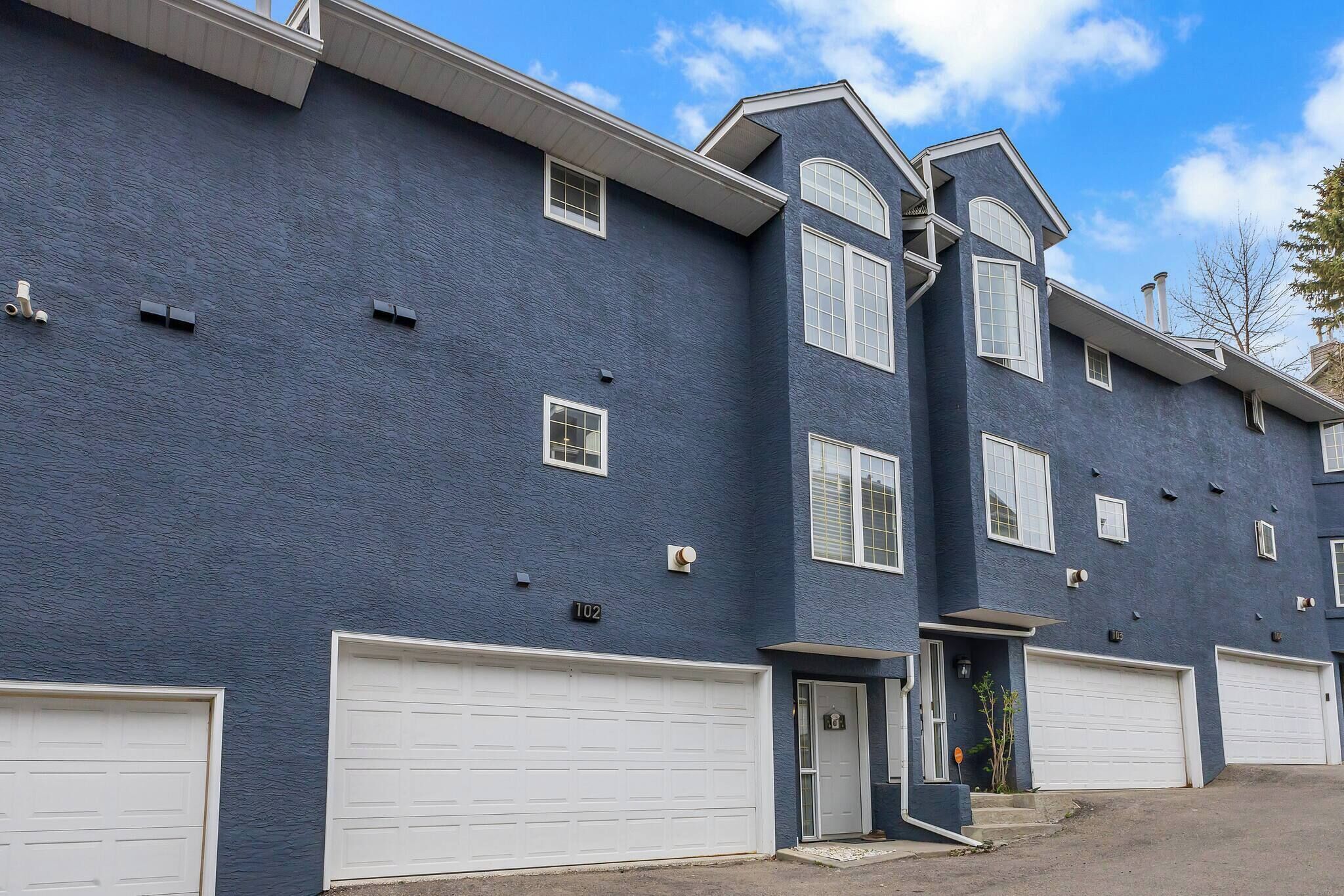 A two-story residential building with a dark blue exterior, white garage doors, and a small front porch.