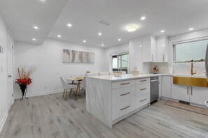 A modern kitchen with white cabinetry, a central island, and a dining area with a table and chairs.
