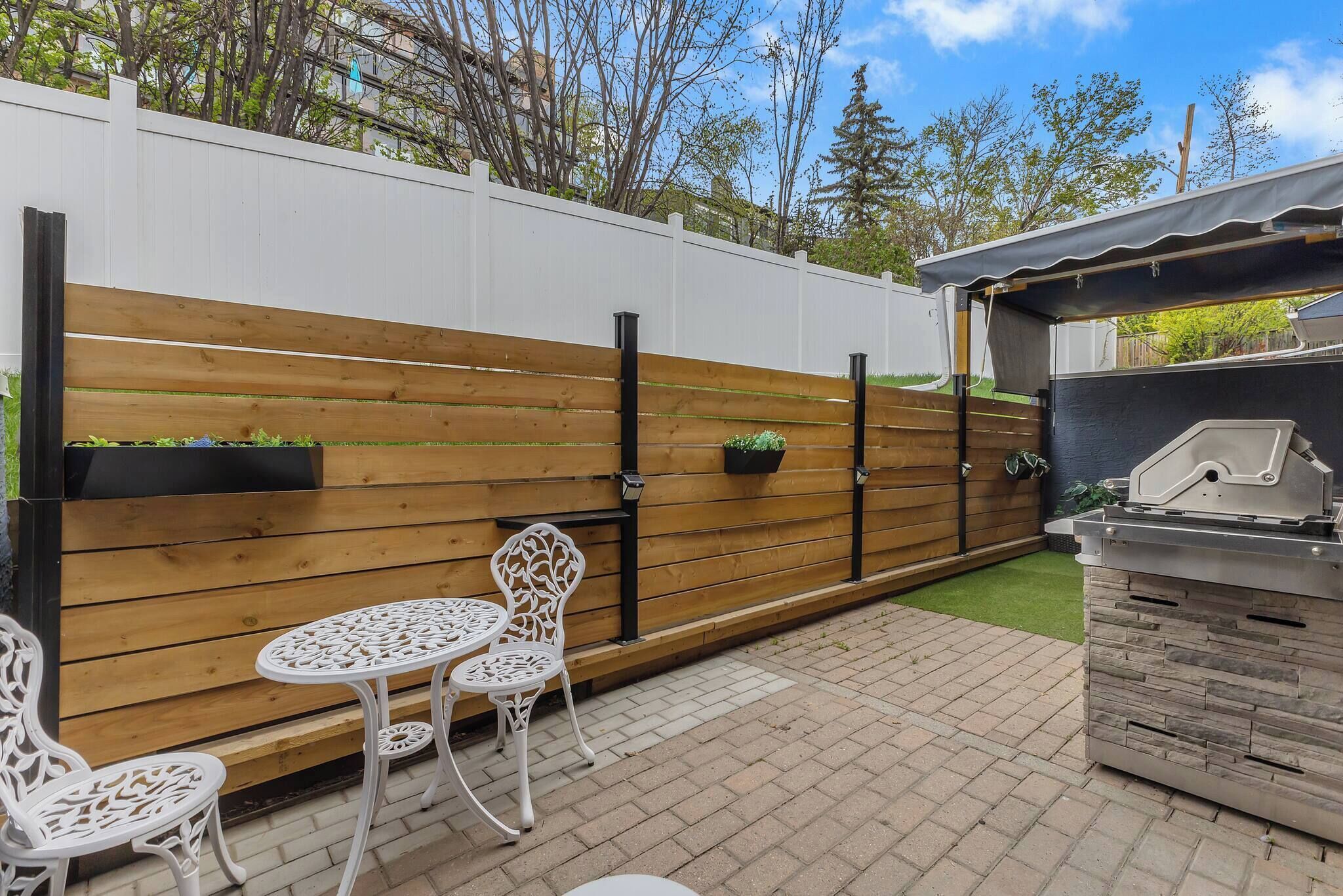 Une terrasse avec une clôture en bois, deux chaises blanches, une petite table et un barbecue.