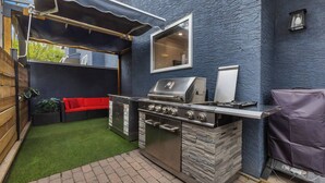 Patio con una parrilla, un sofá rojo y una ventana pequeña.