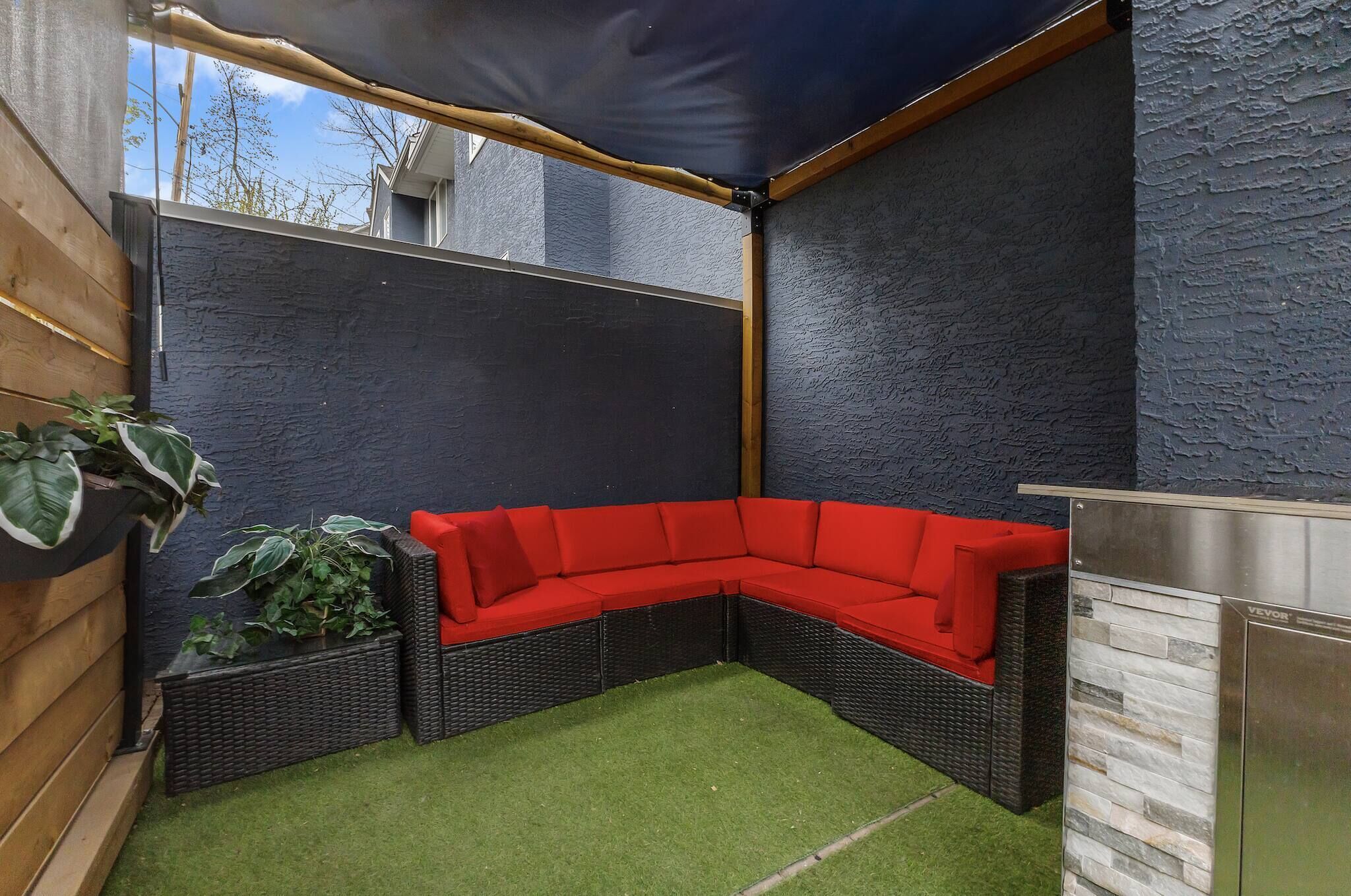 A corner garden with a red sectional sofa, artificial grass, and a dark blue wall.