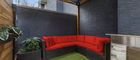 Un jardín en esquina con un sofá seccional rojo, césped artificial y una pared azul oscuro.