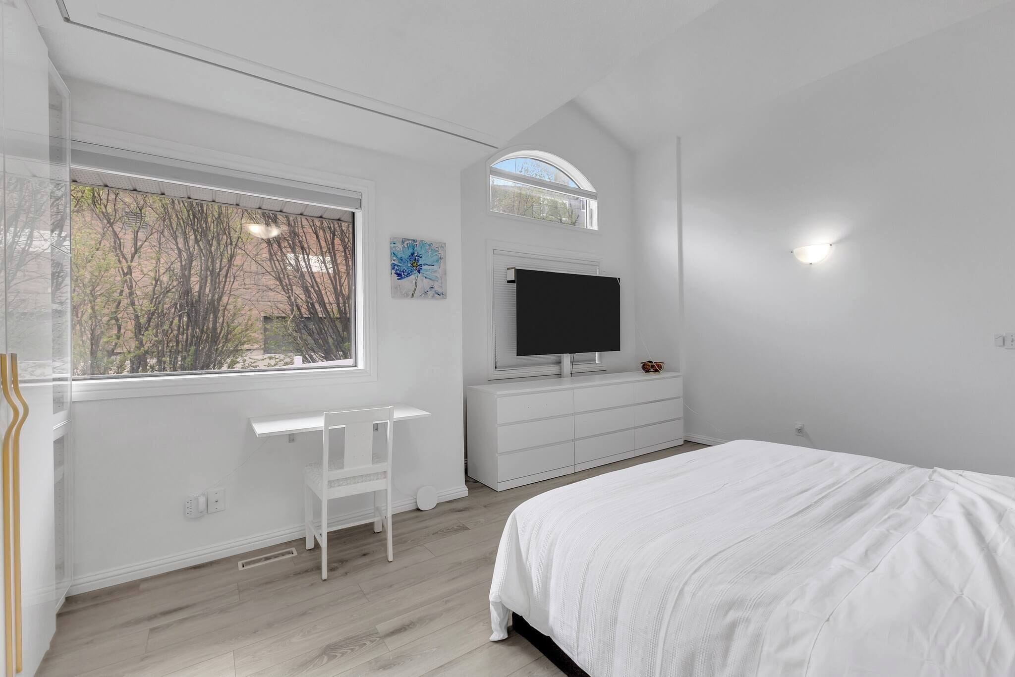 Une chambre à coucher avec un lit, une télévision, un bureau et une fenêtre donnant sur des arbres.